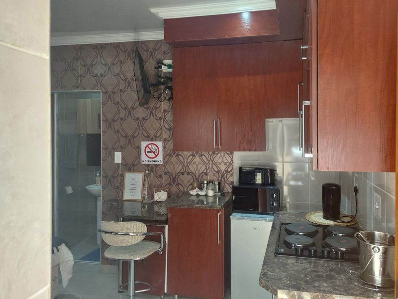 Compact kitchen featuring dark wood-look cabinetry, granite-style countertops, and an integrated electric hob, with an adjacent view into a small bathroom area.