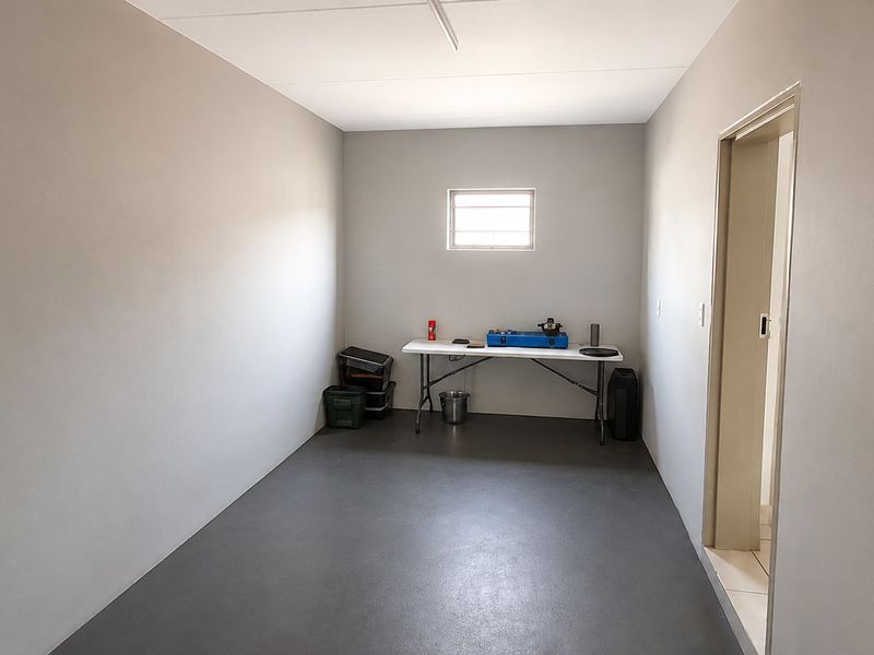 A clean, empty utility room featuring neutral walls, a security window, and durable painted concrete flooring, suitable for storage or a workspace.