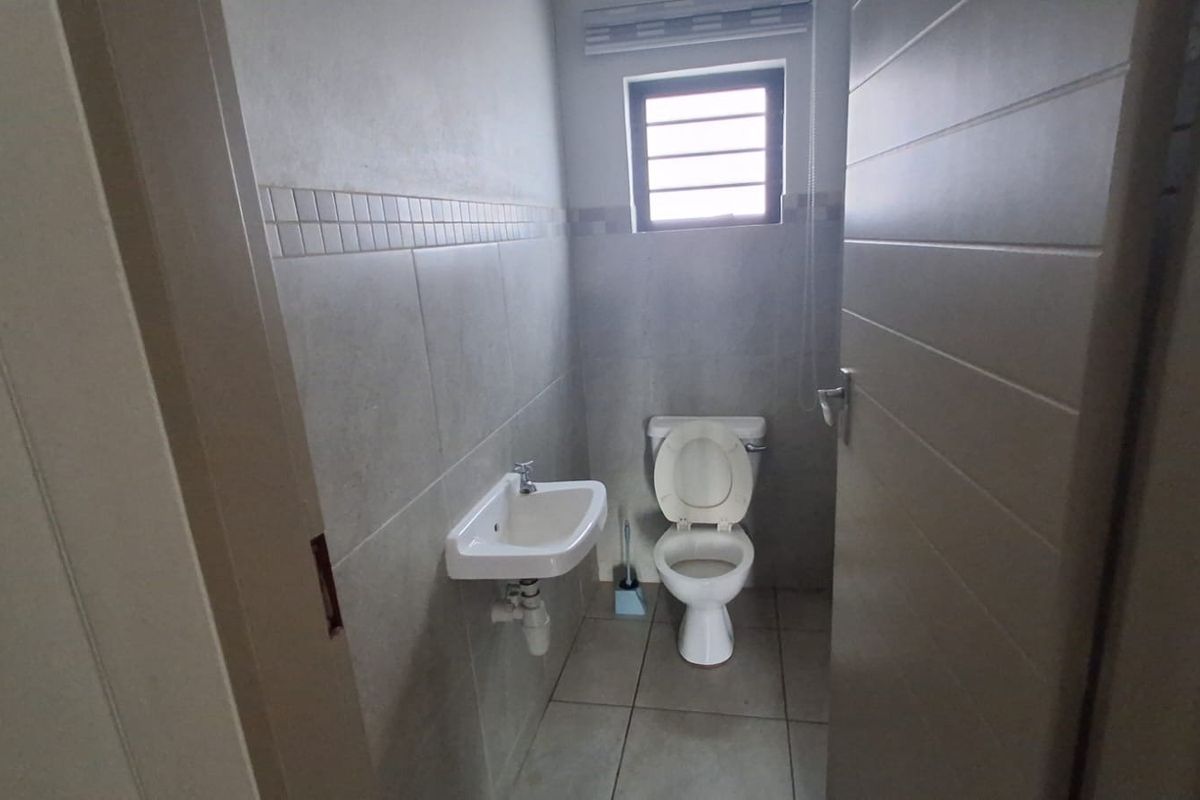 A compact guest bathroom featuring neutral wall and floor tiles, a wall-mounted basin, and a standard toilet.