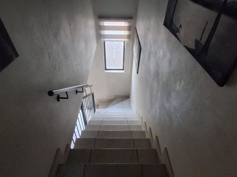 A functional staircase featuring tiled steps, a metal handrail, and a window providing natural light to the hallway area.
