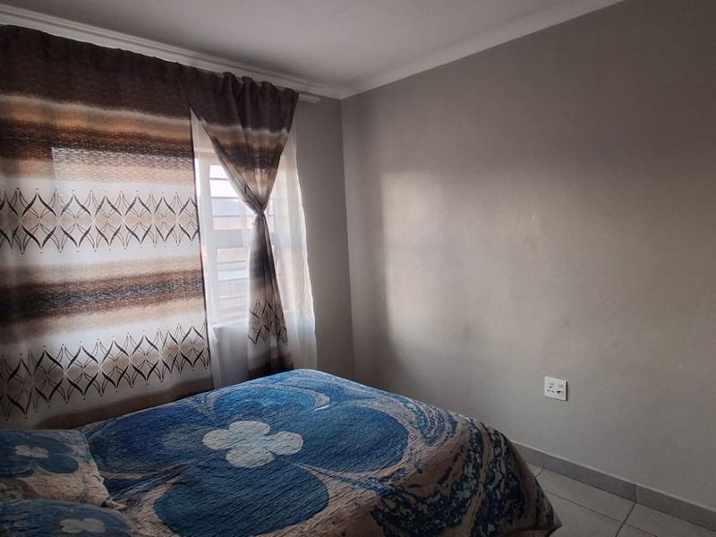 A standard bedroom featuring tiled flooring, neutral wall finishes, and a window with curtain fixtures.