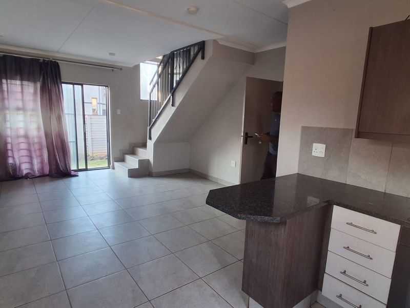 Open-plan living area featuring tiled floors, a compact kitchen with granite countertops, and a staircase leading to the upper level.