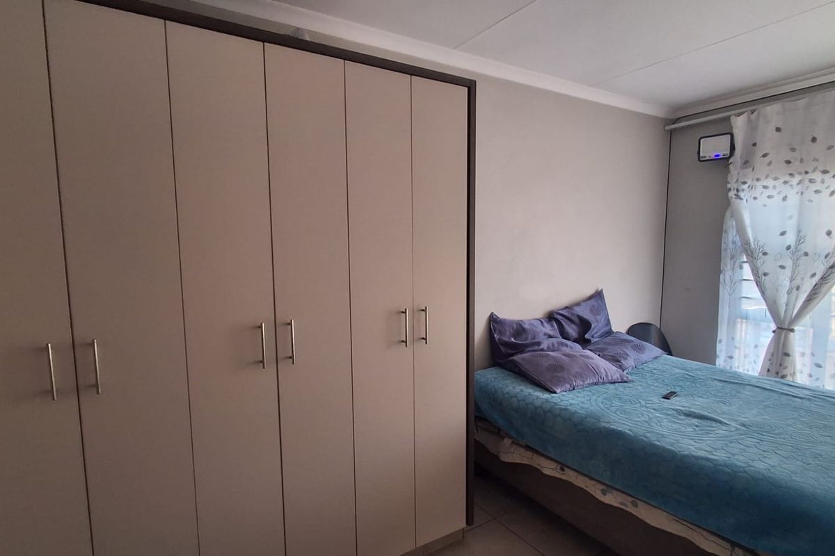 A bedroom featuring a large built-in wardrobe with modern handles and tiled flooring.