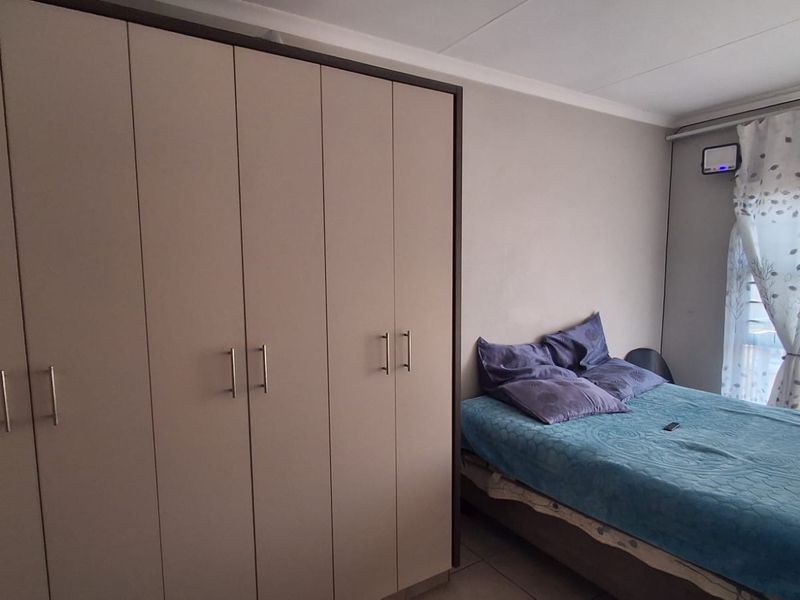 A bedroom featuring a large built-in wardrobe with modern handles and tiled flooring.