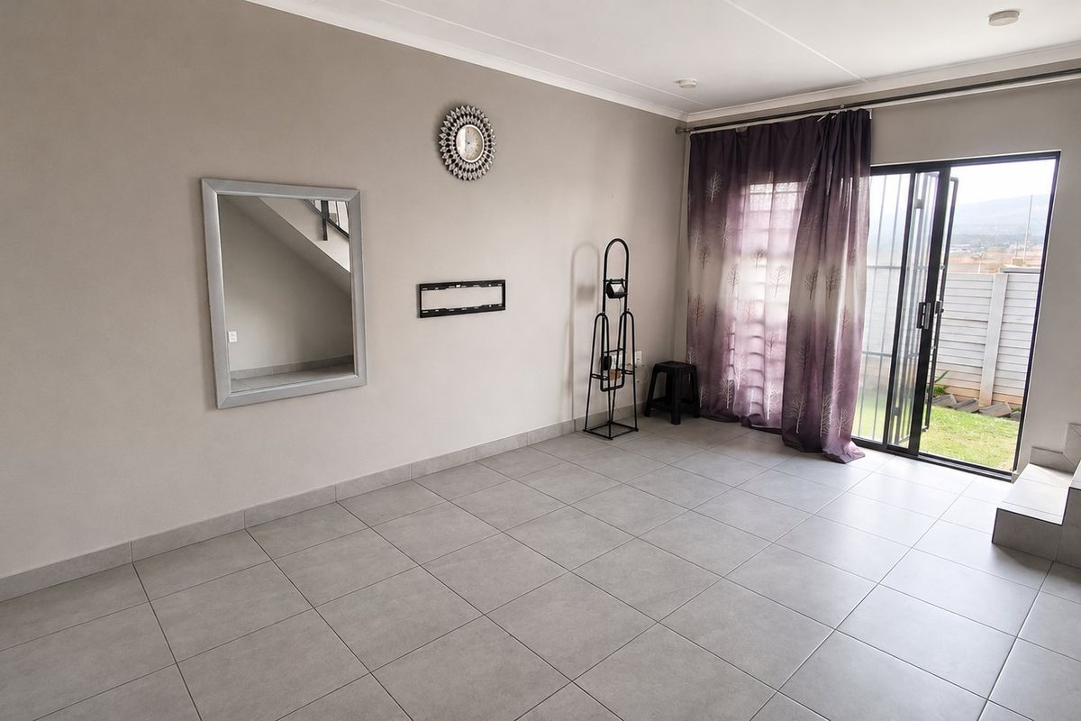 A spacious, neutral-toned living area featuring tiled flooring, a staircase, and a sliding glass door providing direct access to the outdoor garden space.