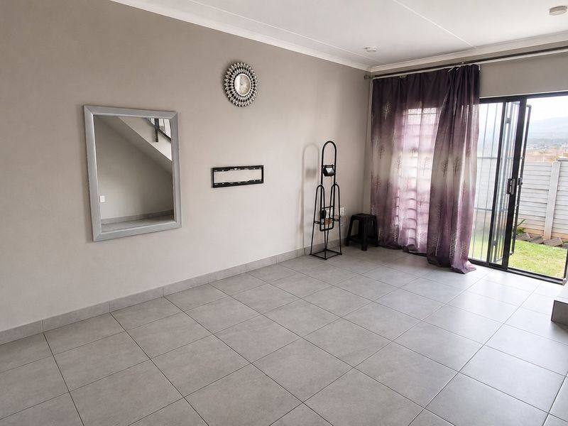 A spacious, neutral-toned living area featuring tiled flooring, a staircase, and a sliding glass door providing direct access to the outdoor garden space.