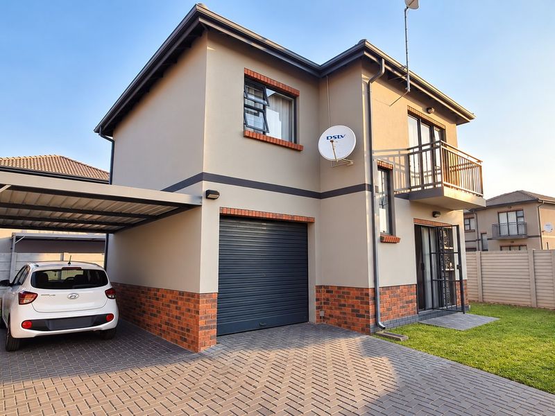 A modern two-story residential property featuring a brick and plaster facade, a paved driveway, a covered carport, and an upper-level balcony.