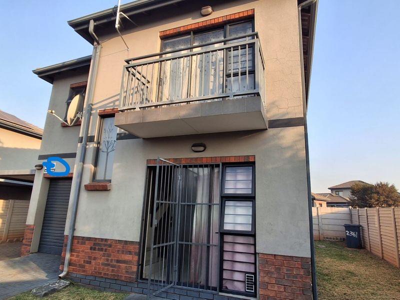 Rear view of a two-story residential property featuring a balcony with metal balustrade, security gate, and a private fenced garden area.