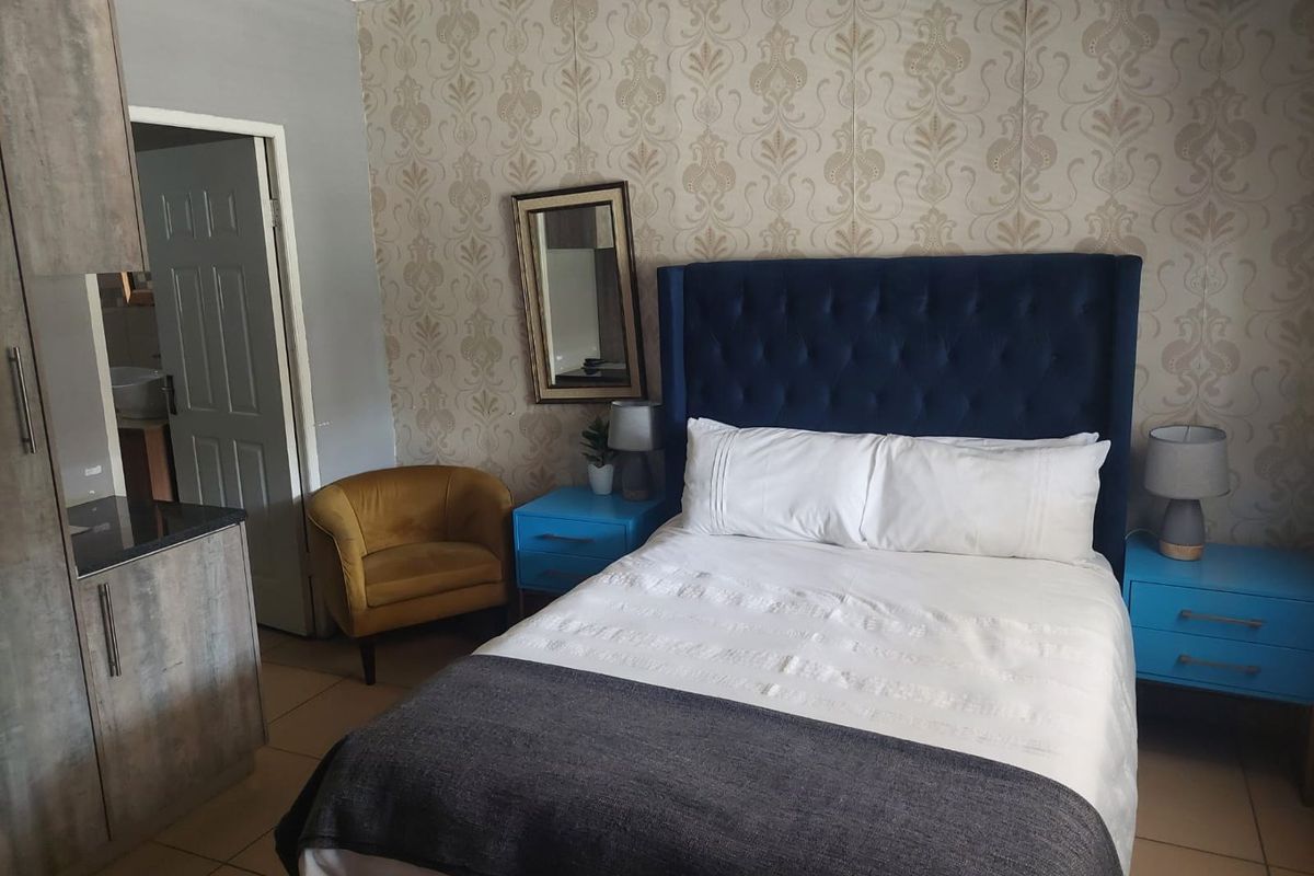 A bedroom featuring tiled flooring, built-in cabinetry, and decorative wallpaper, with an adjoining door leading to an en-suite bathroom.