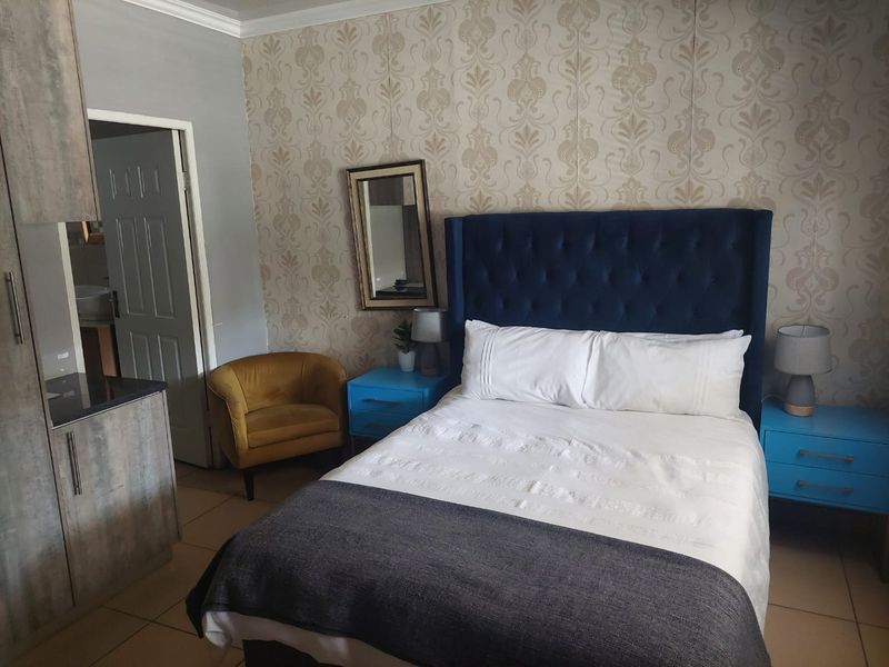 A bedroom featuring tiled flooring, built-in cabinetry, and decorative wallpaper, with an adjoining door leading to an en-suite bathroom.