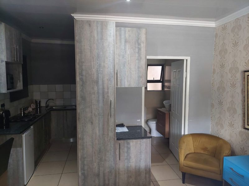 Open plan living area featuring modern wood-look cabinetry, granite countertops, and tiled flooring, with direct access to an adjoining bathroom.