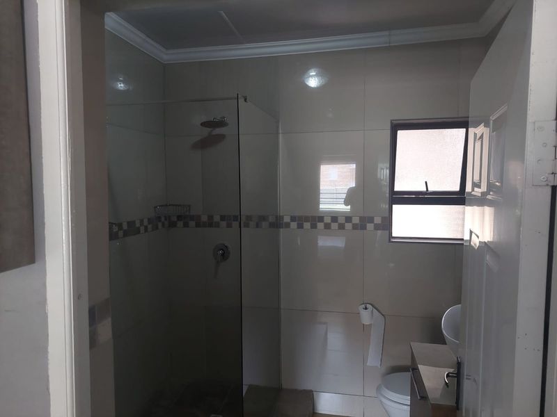 A functional bathroom featuring a glass-enclosed shower, tiled walls with a decorative border, a vanity unit with a basin, and a toilet.