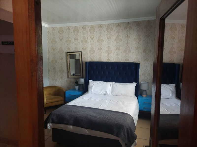 A bedroom featuring patterned wallpaper, tiled flooring, and a mirrored wardrobe door, viewed from the doorway.