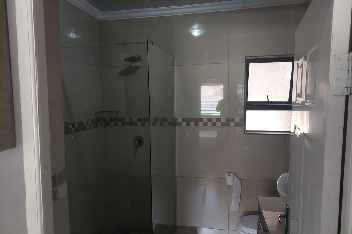 A functional bathroom featuring a glass-enclosed shower, vanity cabinet with basin, and neutral wall tiling.