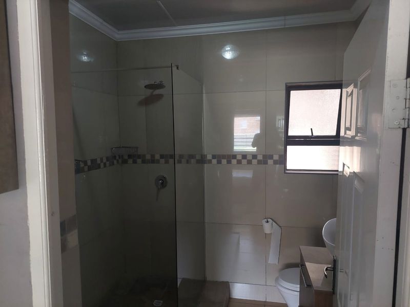 A functional bathroom featuring a glass-enclosed shower, vanity cabinet with basin, and neutral wall tiling.