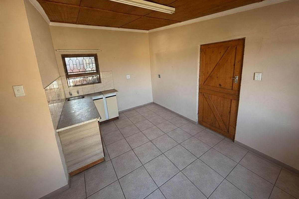 A compact, empty kitchen area featuring tiled floors, timber ceiling, built-in cabinetry with a sink, and a solid timber door.