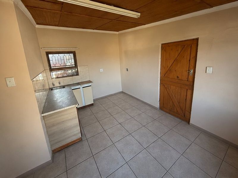 A compact, empty kitchen area featuring tiled floors, timber ceiling, built-in cabinetry with a sink, and a solid timber door.
