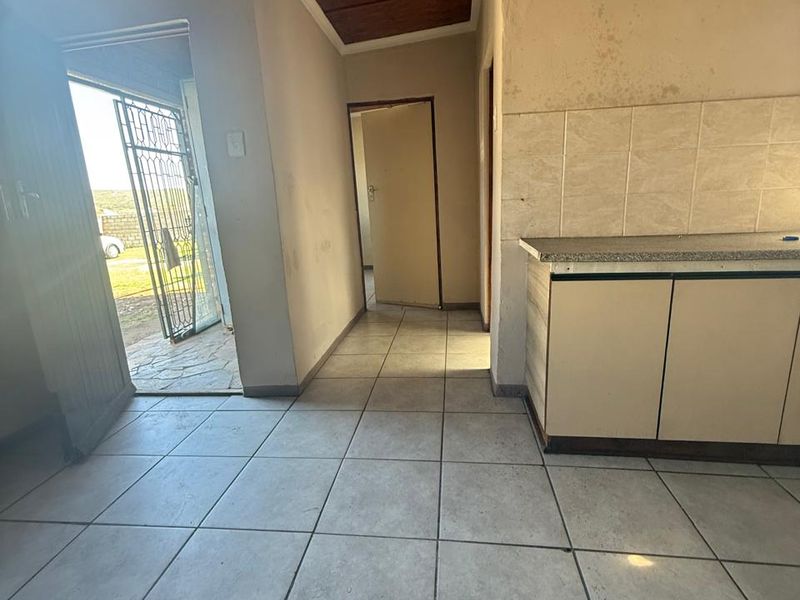 A basic kitchen area featuring tiled flooring, built-in cabinetry, and a tiled splashback, requiring cosmetic updates and repairs to wall and ceiling finishes.
