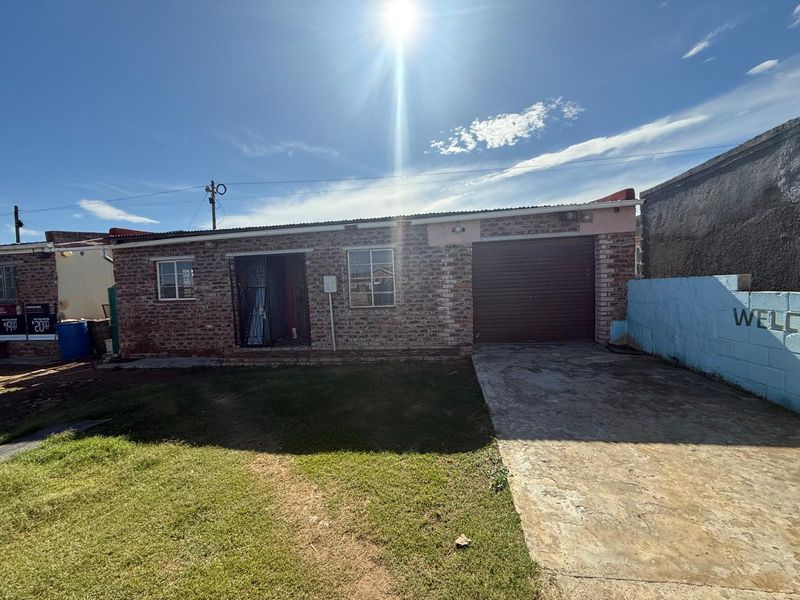 Front view of a single-story face brick house featuring a roller shutter garage door, concrete driveway, and a small front lawn.