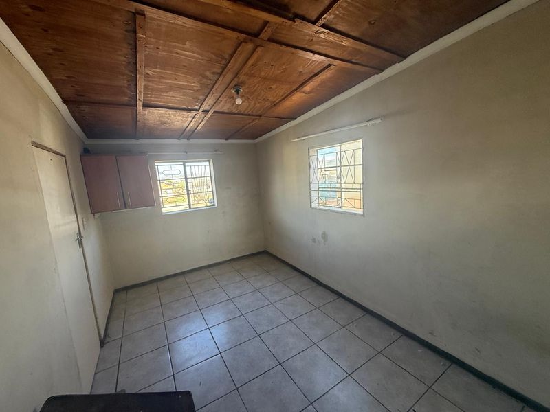 An empty bedroom featuring tiled flooring, a wooden panel ceiling, and security bars on the windows, requiring cosmetic updates to improve its condition.