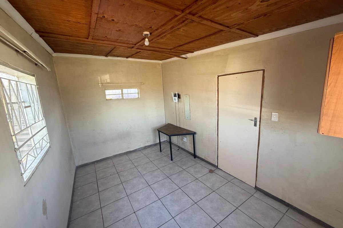 An empty bedroom featuring tiled flooring and a wooden panel ceiling, requiring cosmetic updates and wall repairs to improve its overall condition.