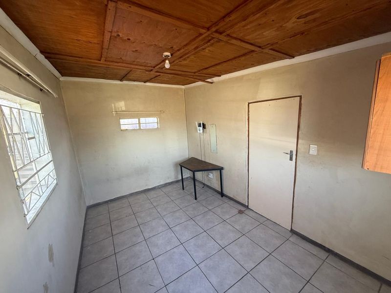 An empty bedroom featuring tiled flooring and a wooden panel ceiling, requiring cosmetic updates and wall repairs to improve its overall condition.