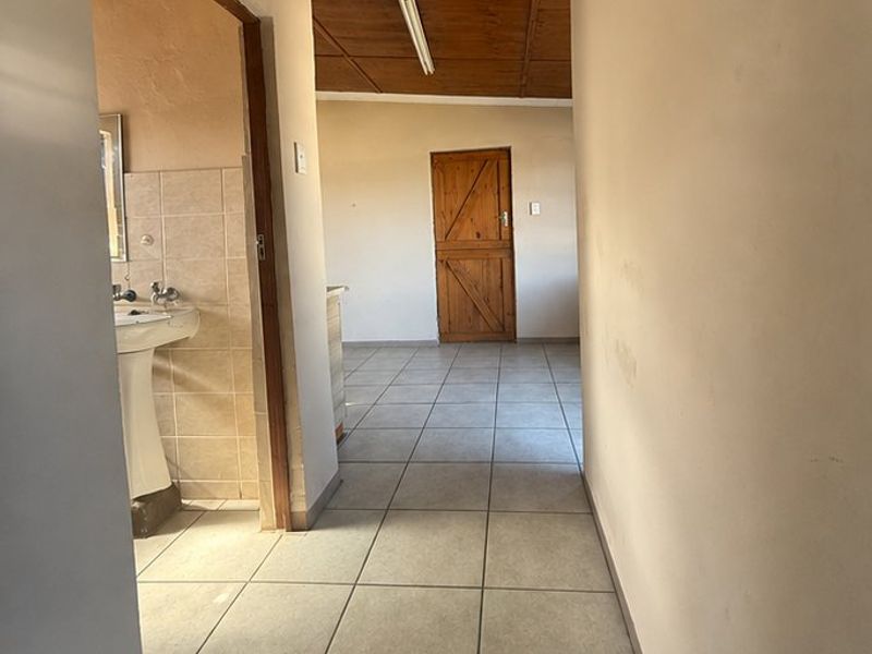 A vacant hallway featuring tiled flooring and a timber ceiling, leading to an adjacent bathroom area with a pedestal basin.