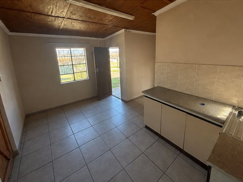 A compact, empty kitchen featuring tiled flooring, laminate countertops, a stainless steel sink, and a timber-paneled ceiling with direct access to the exterior.