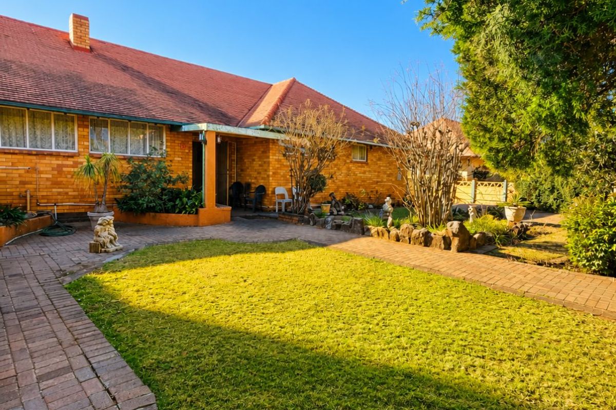 Rear view of a brick house featuring a tiled roof, covered patio area, and a well-maintained garden with brick paved pathways.
