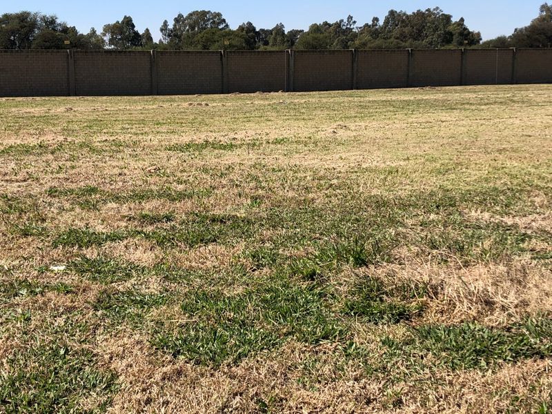 A view of a vacant residential plot featuring a level grass surface and a solid perimeter boundary wall.