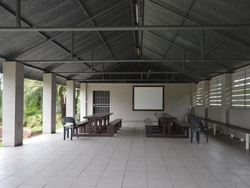A spacious covered outdoor patio area featuring tiled flooring, concrete pillars, and a metal roof structure, suitable for large gatherings or events.