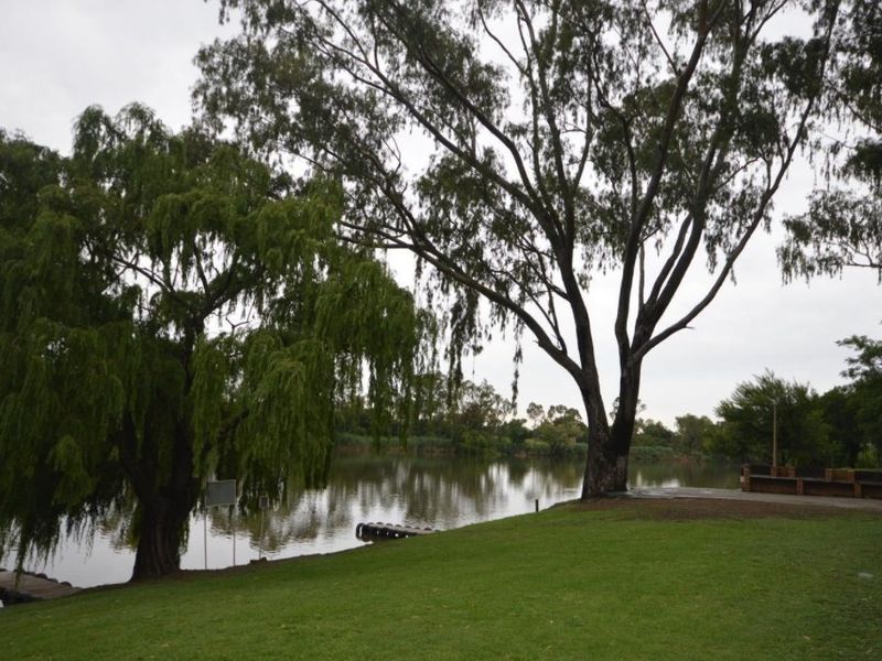 A scenic view of a tranquil lakefront property featuring mature trees, a well-maintained grassed lawn, and direct water access.