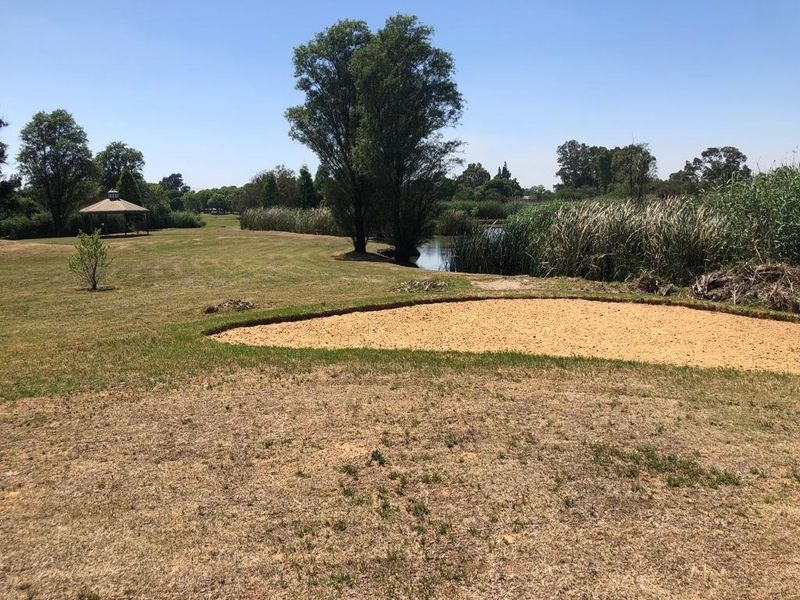 A scenic view of a residential garden featuring a sand bunker, a small pond, and a gazebo set within a landscaped outdoor area.