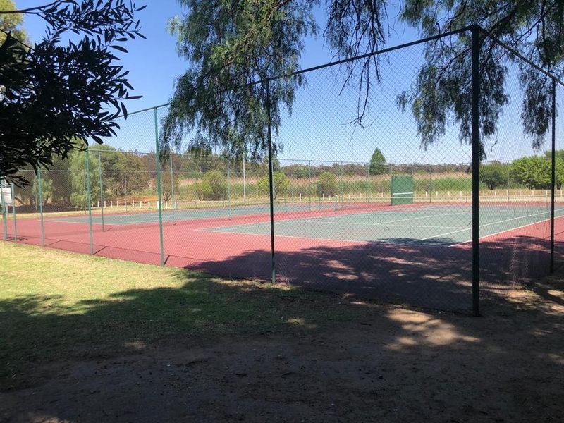 A fenced outdoor tennis court facility situated on the residential property, featuring a hard court surface and perimeter chain link fencing.