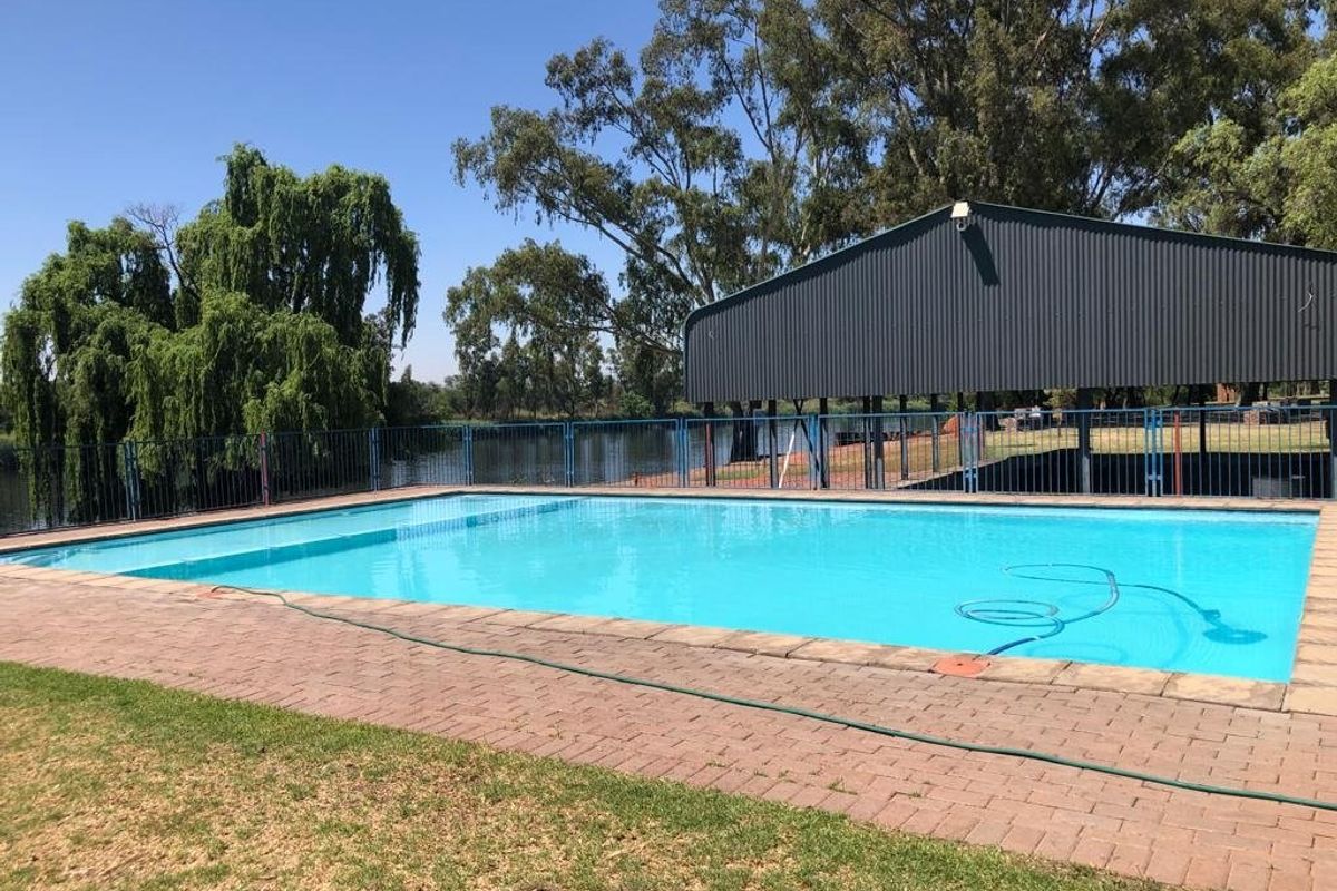 A well-maintained swimming pool area featuring a paved deck, metal perimeter fencing, and an adjacent metal structure overlooking a scenic water feature.