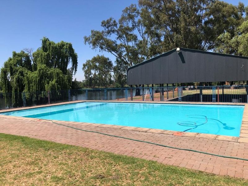 A well-maintained swimming pool area featuring a paved deck, metal perimeter fencing, and an adjacent metal structure overlooking a scenic water feature.