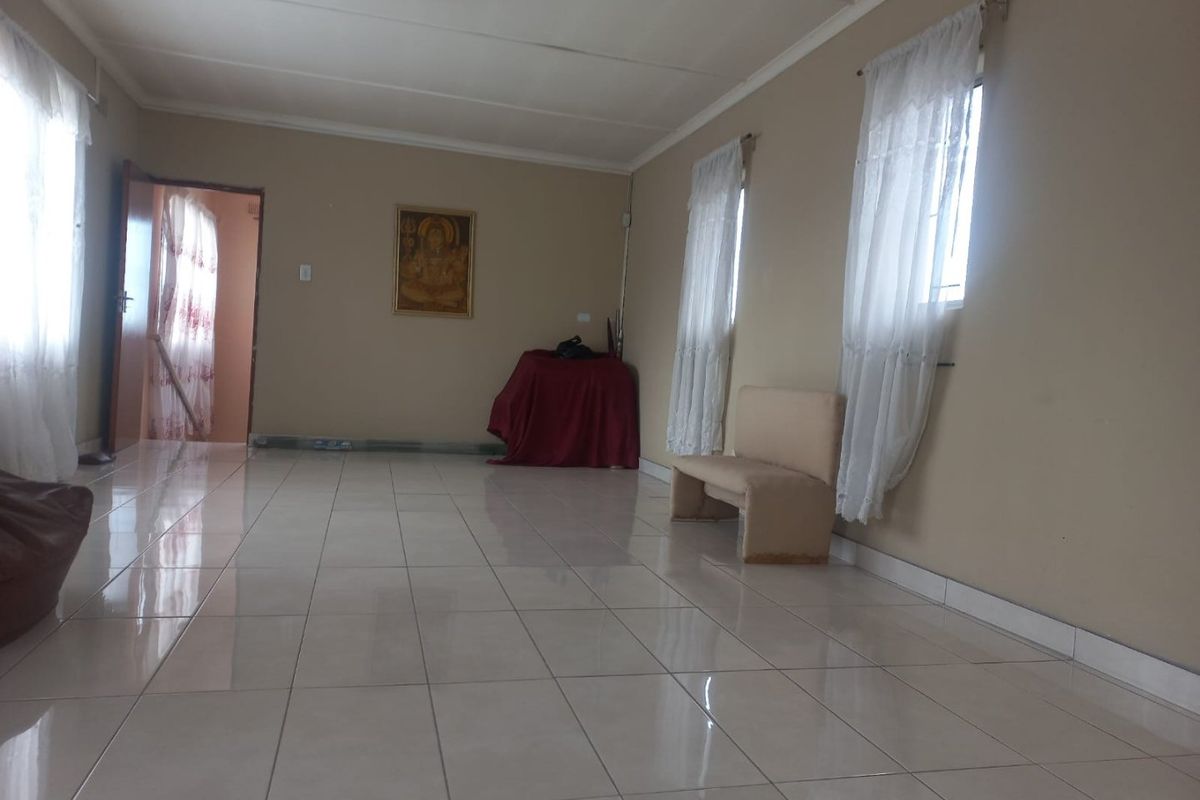 A spacious, empty living area featuring neutral wall tones, tiled flooring, and large windows that provide ample natural light.