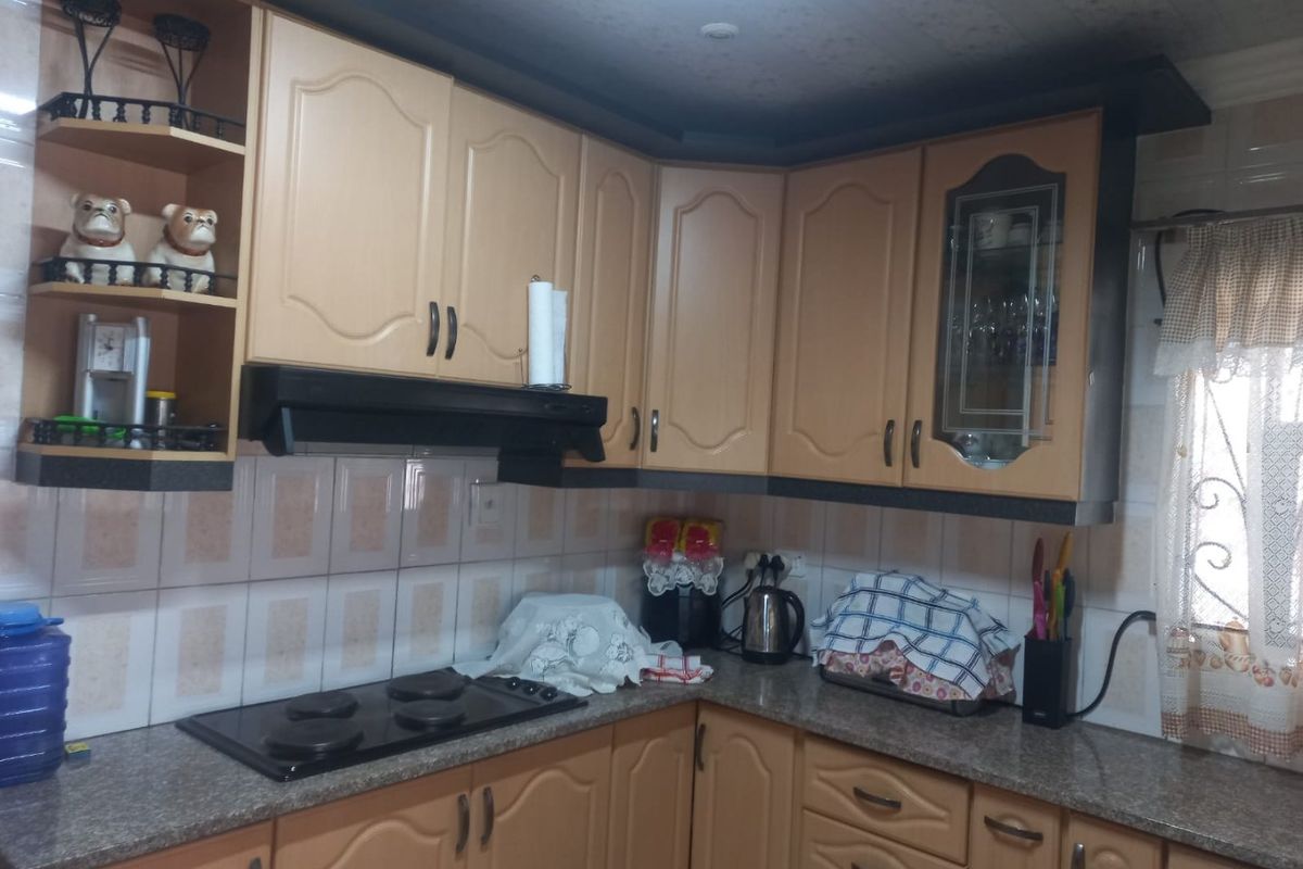 A functional kitchen featuring light wood-tone cabinetry, granite countertops, a built-in hob, and an extractor fan with tiled wall finishes.