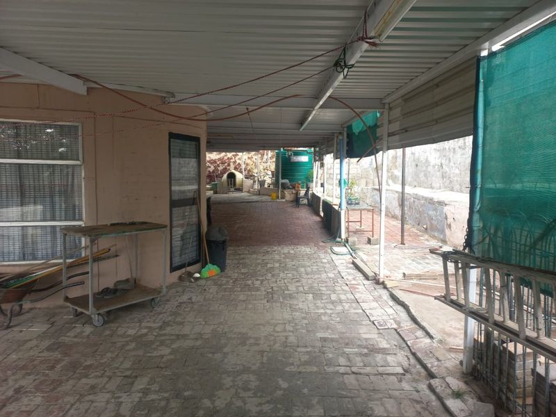 A covered outdoor patio area featuring paved flooring, a corrugated metal roof, and a side retaining wall, offering potential for an outdoor entertainment space.