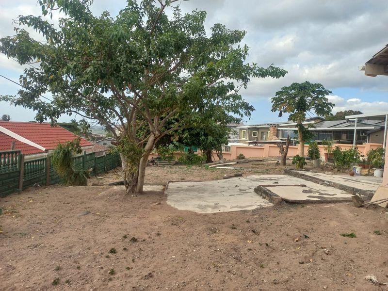 A spacious rear garden area featuring a concrete patio slab, mature trees, and perimeter walling, offering significant potential for landscaping and outdoor improvement.