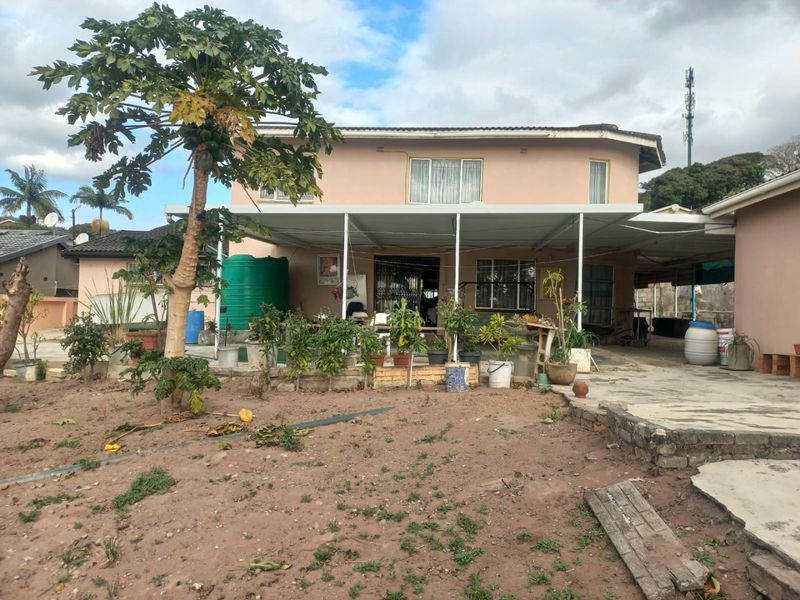 Rear view of the property featuring a covered patio area, concrete paving, and a water storage tank set within a large garden space.