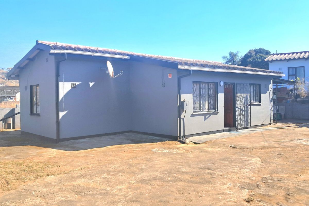 Rear view of a single-story residential house featuring a grey painted exterior, tiled roof, and a concrete yard area.