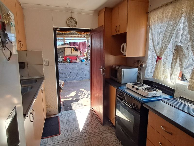A compact kitchen featuring built-in cabinetry, a double sink, and a freestanding stove, with direct access to an outdoor area.
