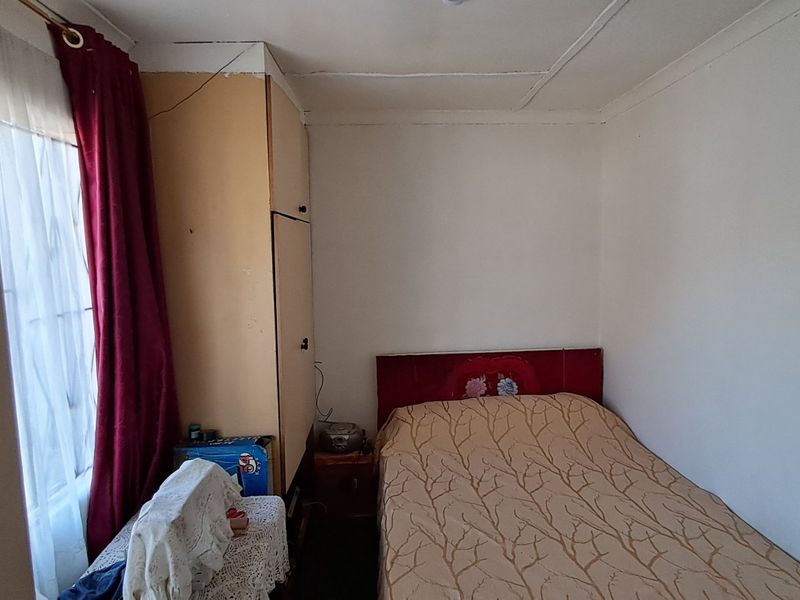 A compact bedroom featuring a built-in wardrobe and standard window, requiring cosmetic updates to the ceiling and wall finishes.