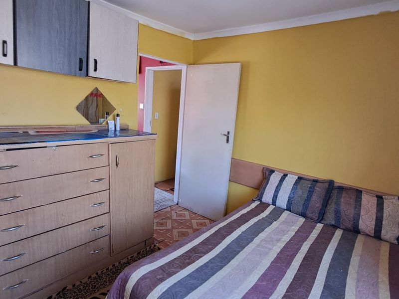 A bedroom featuring built-in wall cabinetry and a standard internal door, with yellow wall finishes and visible wear on the ceiling and flooring.