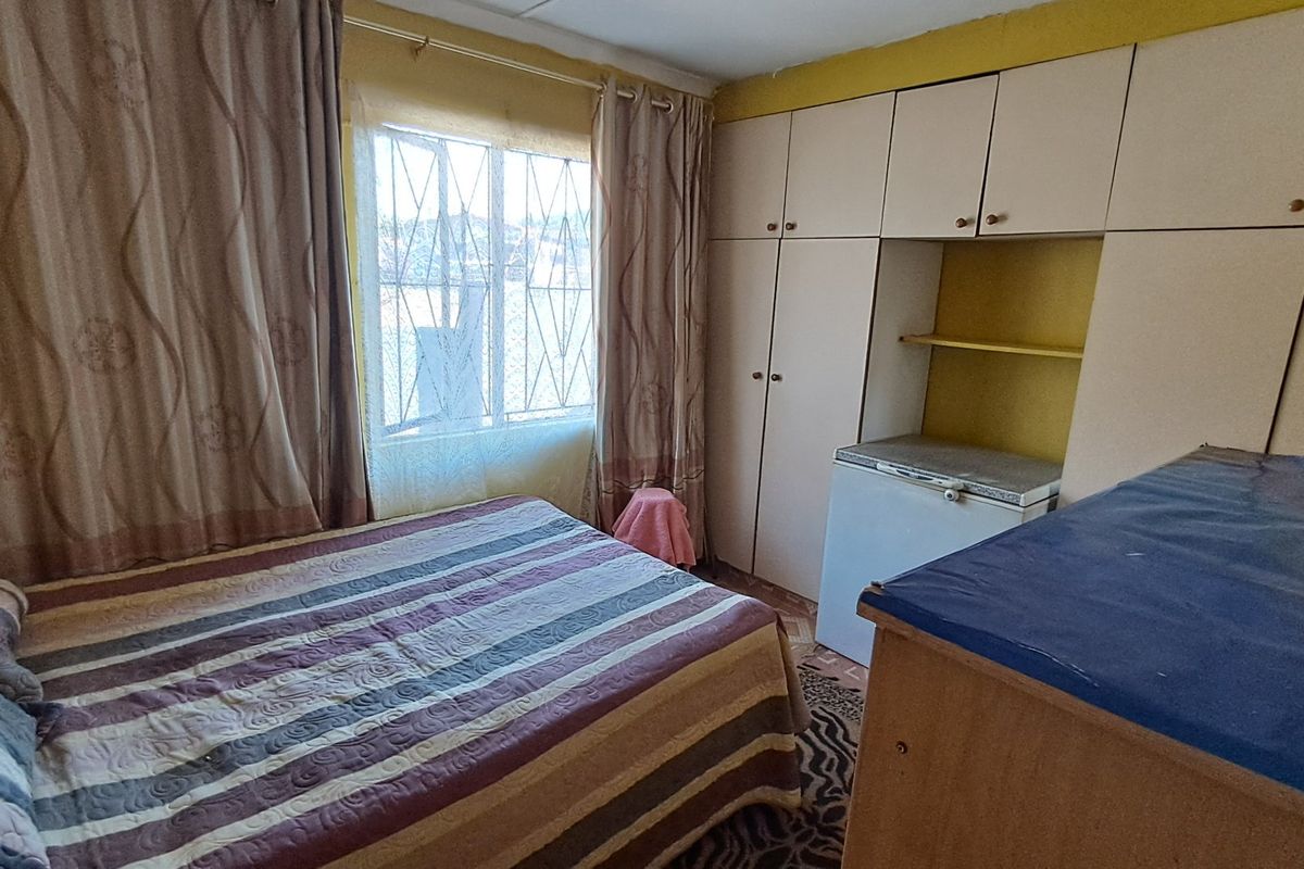A bedroom featuring built-in cupboards and a window with security bars, offering a functional space with potential for cosmetic updates.