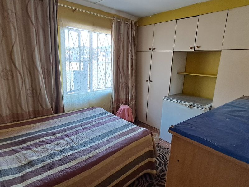 A bedroom featuring built-in cupboards and a window with security bars, offering a functional space with potential for cosmetic updates.