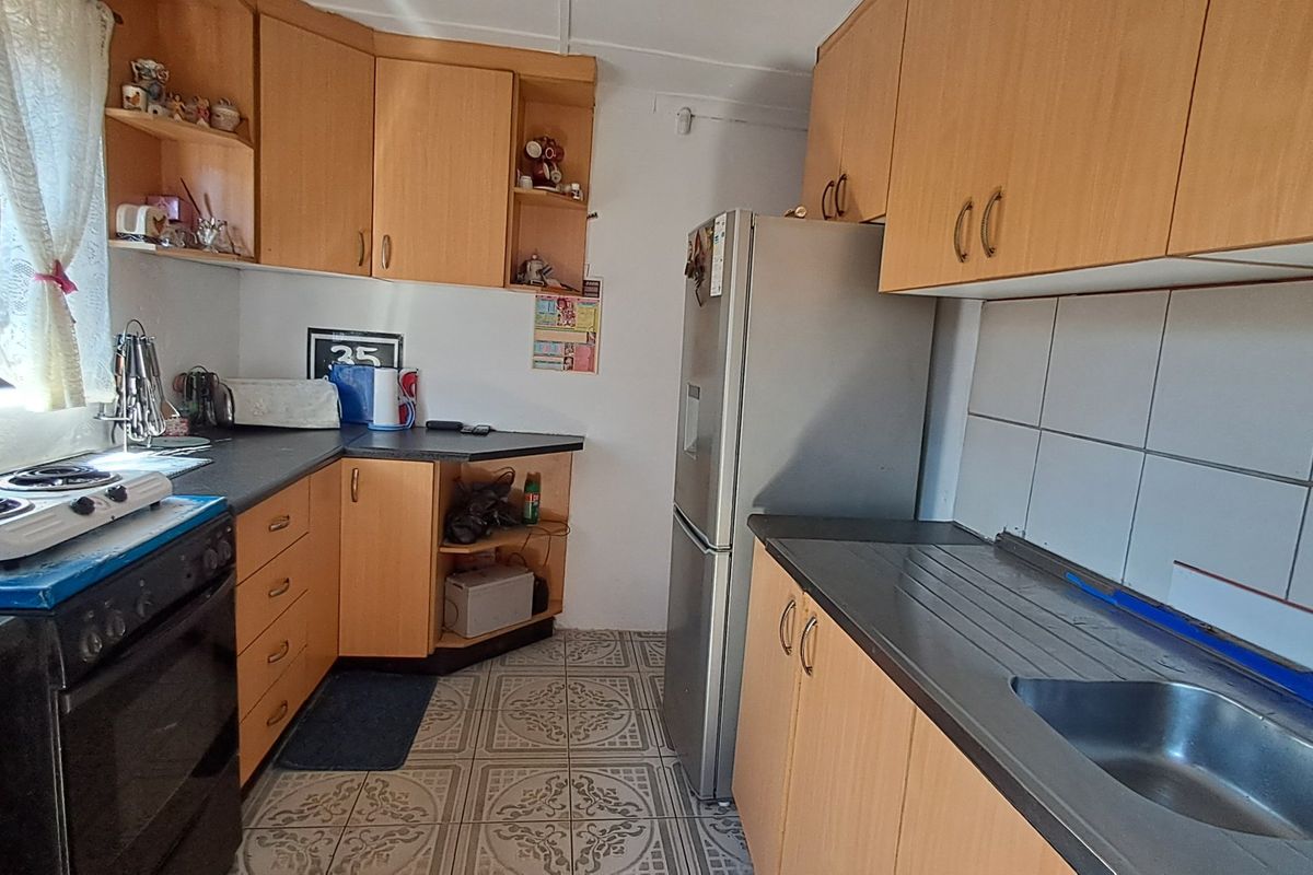 A functional kitchen featuring laminate cabinetry, tiled backsplash, and patterned floor tiles, offering a dated aesthetic ready for modernization.