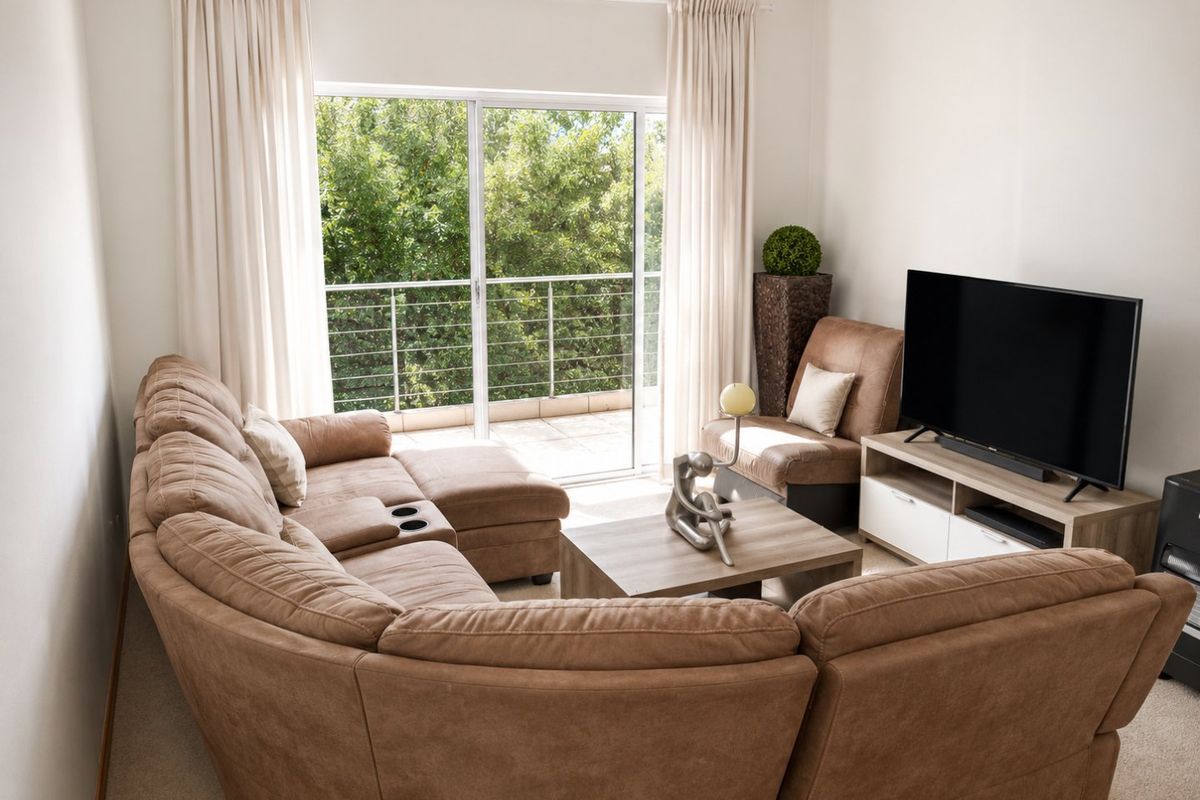 A comfortable living room featuring carpeted flooring and a large sliding glass door that opens onto a private balcony with green views.