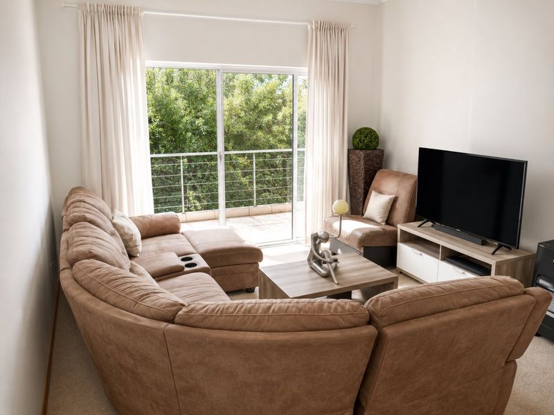 A comfortable living room featuring carpeted flooring and a large sliding glass door that opens onto a private balcony with green views.